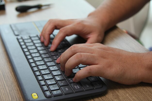 Eine Person tippt auf einem Laptop mit Stift und Bleistift auf dem Tisch.
