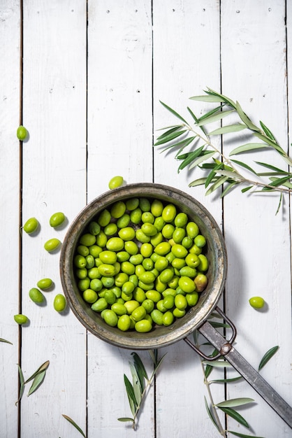 Eine Pfanne mit grünen Bio-Oliven gefüllt, um Olivenöl auf weißem Hintergrund zuzubereiten