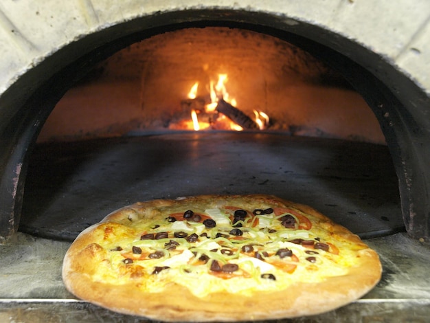 Eine Pizza in einem Holzofen mit einem Feuer im Hintergrund.