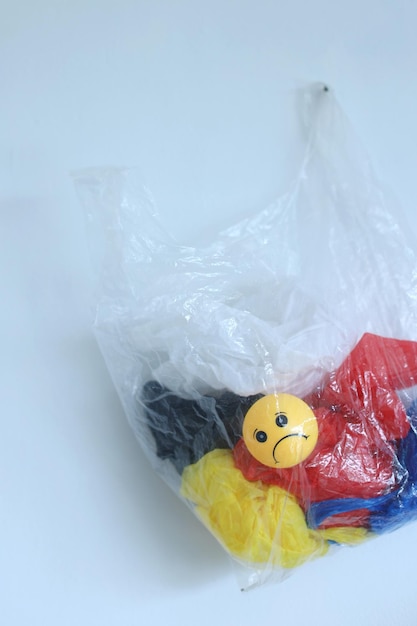 Eine Plastiktüte und ein trauriges Emoticon hängen am weißen Wandhintergrund. Das Konzept der Plastikumfrage