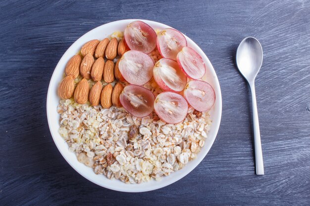 Eine Platte mit Müsli, Mandeln, rosa Trauben auf einem schwarzen hölzernen Hintergrund.