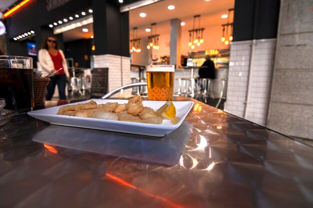 Foto eine portion chocos fritos, gebratene kalmar und ein glas bier auf einem aluminiumtisch