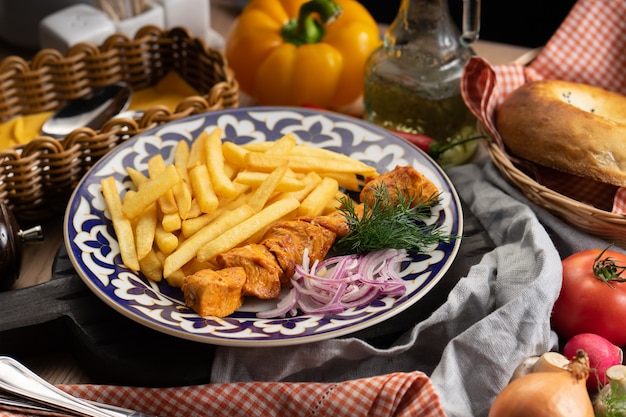 Eine Portion Hühnchen-Schaschlik mit Pommes Frites, Zwiebeln und Dill in einem Teller mit einem traditionellen Usbeken