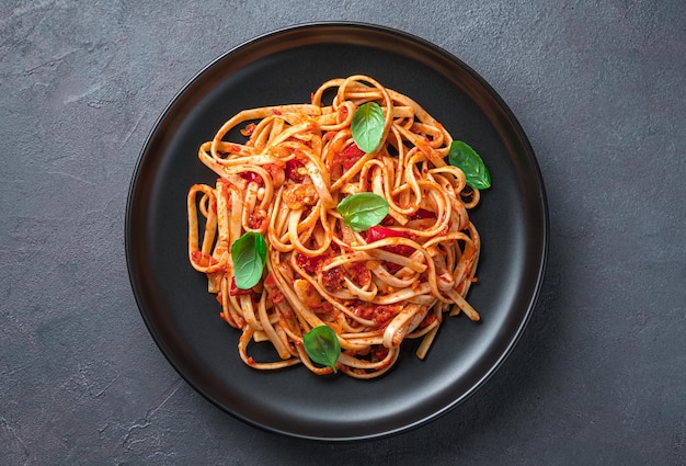 Eine Portion Linguini-Nudeln mit Tomaten und Basilikum in Nahaufnahme auf graublauem Hintergrund