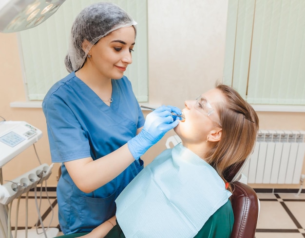 Eine positive dunkelhaarige Frau sitzt in der Zahnarztpraxis während eines Kontrollzahnarztes, der die Zähne der Frau untersucht