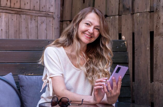 Eine positive reife Frau mit einem Smartphone in den Händen sitzt an einem Café-Tisch