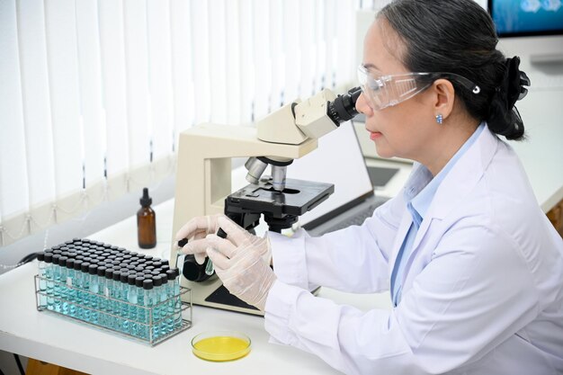 Eine professionelle asiatische Wissenschaftlerin, die eine Virusprobe unter einem Mikroskop untersucht