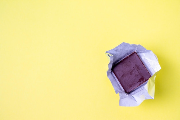 Eine quadratische Minischokolade in einer Verpackung liegt auf einem gelben Hintergrund, eine Kopie des Raums