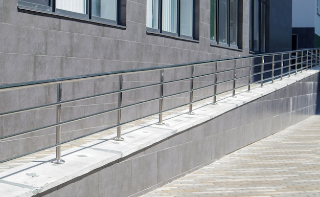 Eine Rampe mit Edelstahlhandläufen für Rollstühle, Fahrräder und Kinderwagen mit Kindern vor dem Gebäude. Handlauf zum Anheben eines Rollstuhls. Glänzender Handlauf aus Edelstahl.