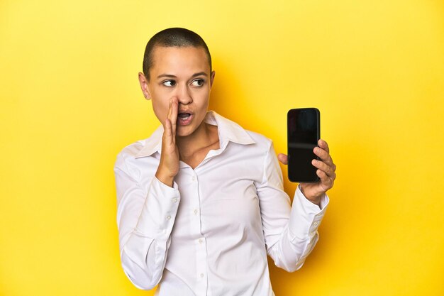 Eine rasierte Frau mit einem mobilen gelben Hintergrund erzählt eine geheime heiße Breaking News