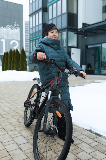 Eine reife europäische Frau, gekleidet in einen Wintermantel, fährt mit dem Fahrrad durch die Straßen der Stadt