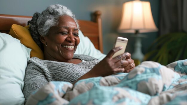 eine reife, lächelnde afroamerikanische Frau, die im Bett liegt und auf ein Handy schaut