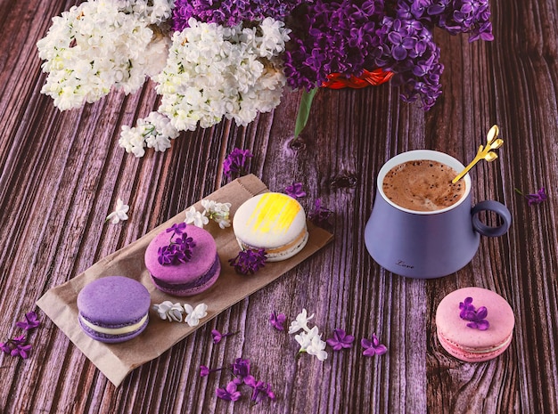 Eine Reihe bunter Makronen-Desserts auf dem Tisch und eine graue Tasse Kaffee mit lila Blumen