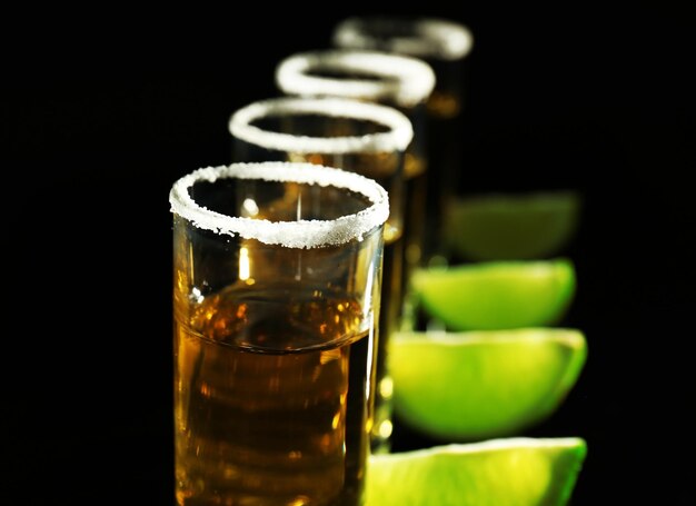 Foto eine reihe goldener tequila-shots mit saftigen limetten und salz auf schwarzem hintergrund