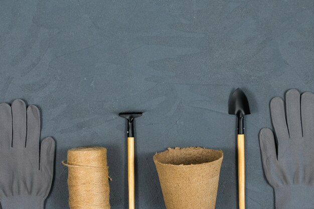 Eine Reihe von Gartengeräten mit Handschuhen und einem Topf zum Umpflanzen von Blumen auf einem grauen Betonstrukturhintergrund Platz für eine Inschrift Ansicht von oben