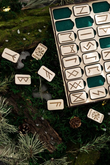 Eine Reihe von Holzrunen in einer Kiste liegen auf dem Moos im Wald. rechteckige Holzplattformen, auf denen skandinavische Runen eingeritzt sind, liegen auf grünem Moos, umgeben von Salz, Zapfen, Tannennadeln und Rinde