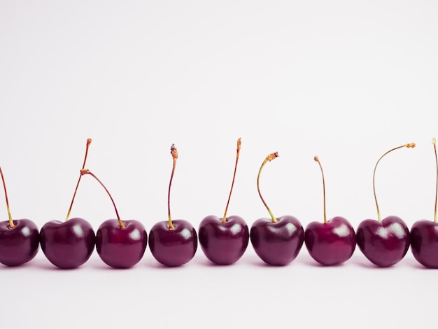 Eine Reihe von Kirschbeeren, die in einer Linie auf einem blassrosa Hintergrund stehen