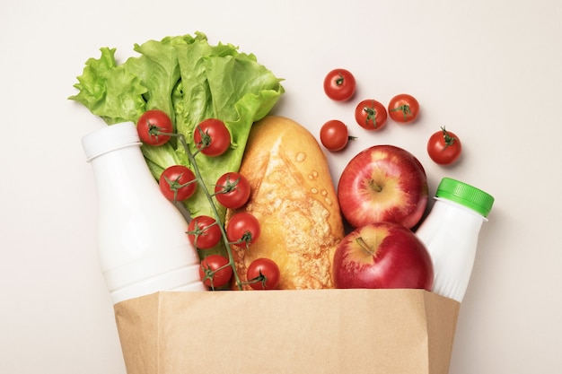 Eine Reihe von Lebensmitteln in einem Karton auf farbigem Hintergrund. Das Konzept der Lebensmittellieferung. Milch in einer Flasche, Kirschtomaten auf einem Ast, Brot, Nudeln, Würstchen, Äpfel, Salatblätter.