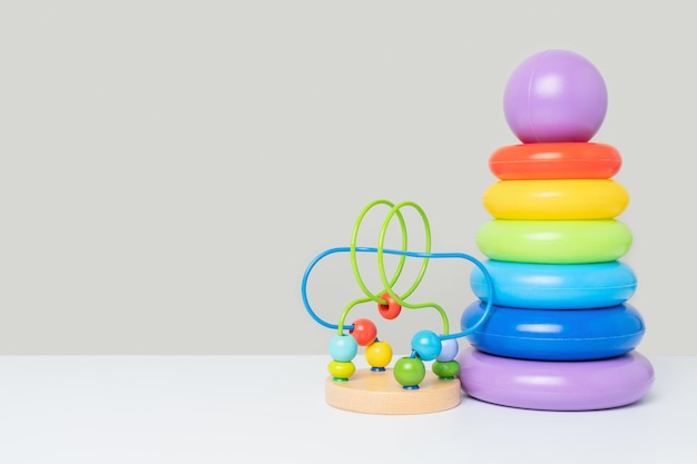 Eine Reihe von Lernspielzeug für Kinder auf grauem Hintergrund Eine farbige Plastikpyramide aus Ringen und ein Labyrinth mit Holzperlen