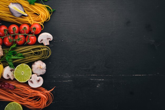 Eine Reihe von Nudeln Nudeln Spaghetti Tagliatelle Fettuccine Farfalle italienische Küche frisches Gemüse und Gewürze auf schwarzem Holzhintergrund Draufsicht Kopierbereich