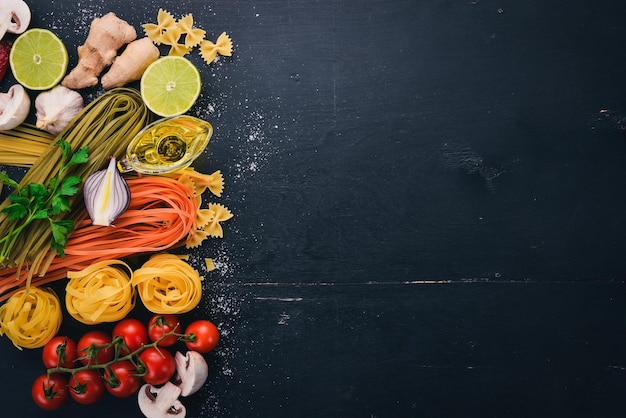 Eine Reihe von Nudeln Nudeln Spaghetti Tagliatelle Fettuccine Farfalle italienische Küche frisches Gemüse und Gewürze auf schwarzem Holzhintergrund Draufsicht Kopierbereich