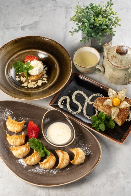 Eine Reihe von schönen Desserts und eine Tasse grüner Tee mit einer Teekanne. Süße Gyoza-Knödel mit frischen Erdbeeren, Mandeltarte mit Eis und gebratener Esterhazy-Kuchen mit Physalis und Minze