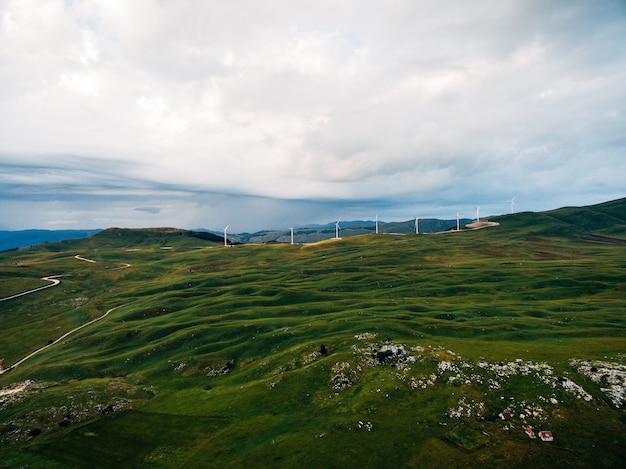 Eine Reihe von Windkraftanlagen auf grünen Hügeln in den Bergen Montenegros gegen den bewölkten regnerischen Himmel