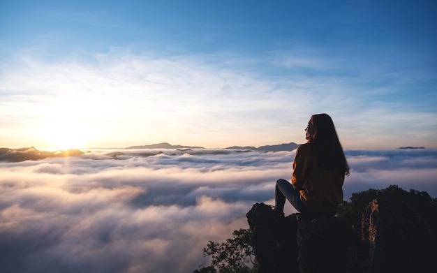 Eine Reisende, die auf dem Berggipfel sitzt und den Sonnenaufgang und das Nebelmeer beobachtet