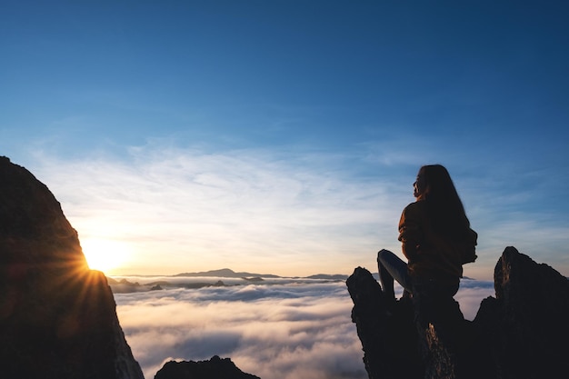 Eine Reisende, die auf dem Berggipfel sitzt und den Sonnenaufgang und das Nebelmeer beobachtet