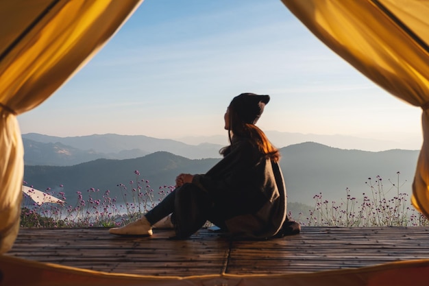 Eine Reisende, die auf einem Holzbalkon sitzt und dabei einen wunderschönen Blick auf die Berge und die Natur außerhalb des Zeltes beobachtet