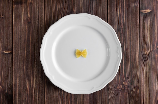 Eine rohe Pasta Farfalle auf weißem Teller auf Holztisch