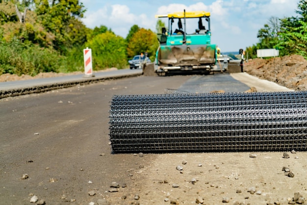 eine rolle aus metallgitter liegt am straßenrand auf dem hintergrund von baugeräten für straßenarbeiten