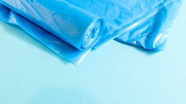 Eine Rolle Plastikmülltüten in Blau auf blauem Grund. Taschen, die für die Unterbringung von Müll konzipiert sind und zu Hause verwendet und in verschiedenen Müllbehältern platziert werden. Platz kopieren.