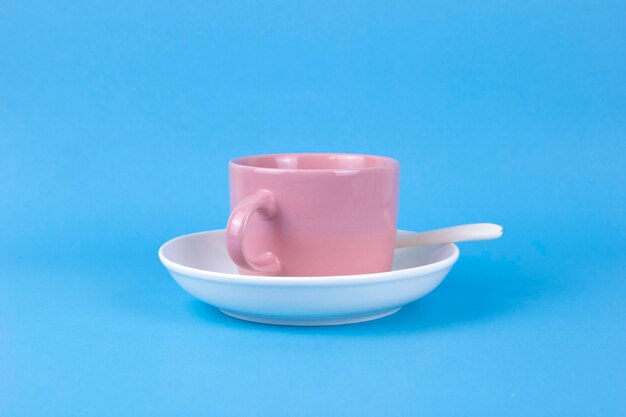 Eine rosafarbene Tasse Kaffee auf wjite Teller und blauem Farbhintergrund