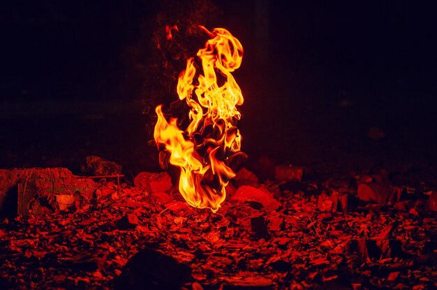 Eine rote Flamme brennenden Feuers erhebt sich aus einem mit Herbstblättern bedeckten Stein.