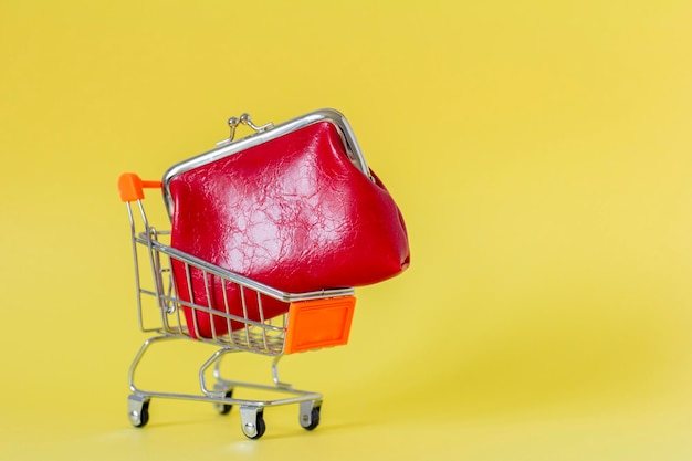 Eine rote Geldbörse in einem Einkaufswagen auf gelbem Hintergrund Ein Symbol für Handel und Verkauf