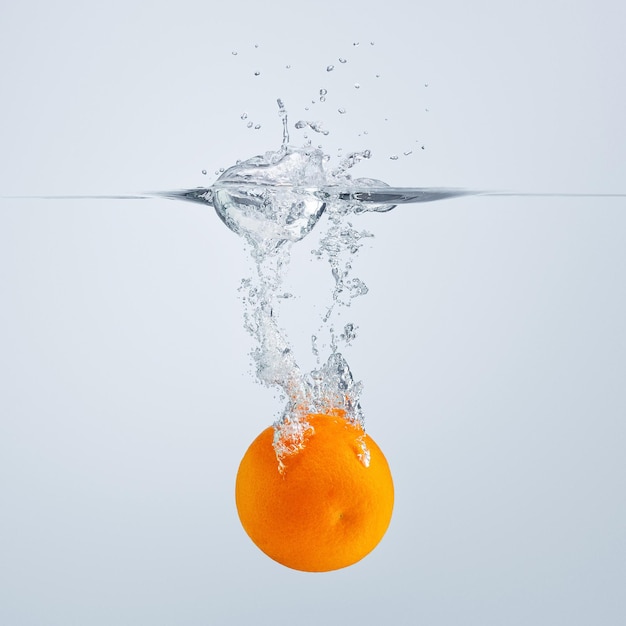 Eine rote Orangenscheibe fällt ins Wasser und wirft viele Spritzer und Tropfen ab.