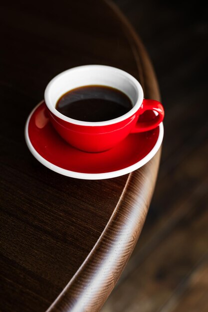 Eine rote Tasse schwarzes Kaffee auf einer Schüssel an der Kante des Holztisches Kopierraum