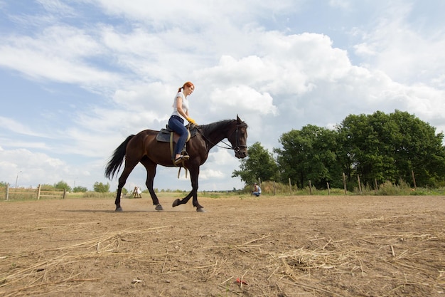 Eine rothaarige Frau, die ein Pferd auf dem Feld reitet, ein grüner Busch auf einem Hintergrund