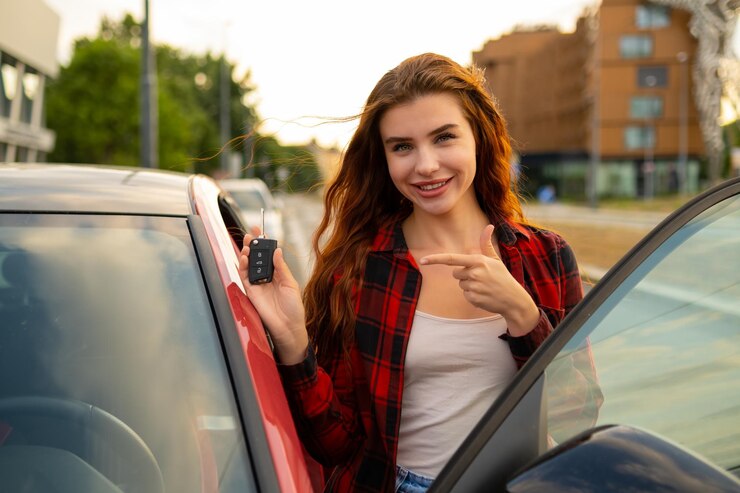 Eine rothaarige Frau in einem Plaidshirt strahlt Glück aus, während sie neben ihrem frisch erworbenen roten Auto posiert und
