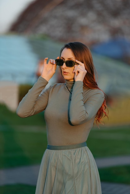 Eine rothaarige Frau in grüner Kleidung überprüft ihre Sonnenbrille