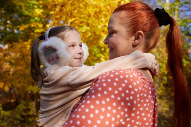 Eine rothaarige glückliche Frau mit einer kleinen Tochter im Arm in einem sonnigen Herbstpark