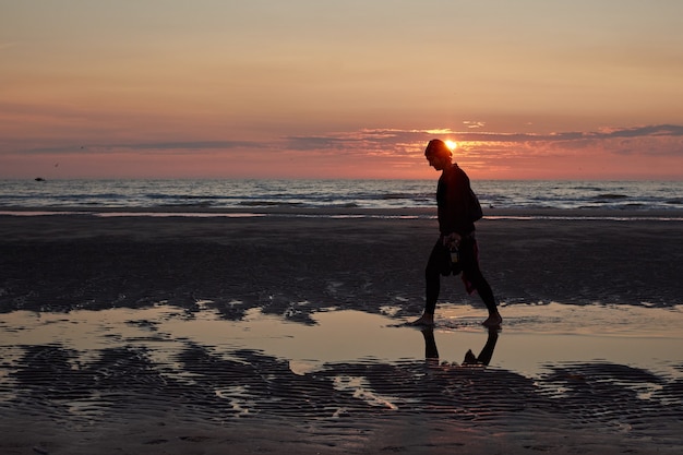 Eine Rückansicht einer Dame, die am Strand spazieren geht und den malerischen Sonnenuntergang genießt