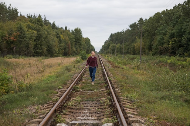 Eine Rückansicht einer jungen Frau, die entlang der Schienen einer Eisenbahnstraße weggeht Das Konzept der Abfahrt