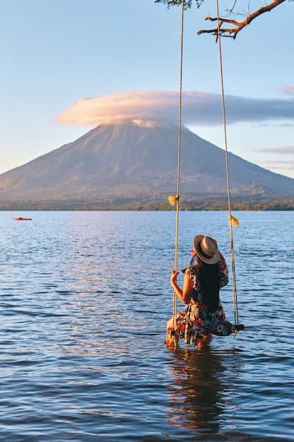 Eine Rückansicht eines jungen Mädchens, das auf einer Schaukel sitzt und den Vulkan Concenpcion auf der Insel Ometepe Nicaragua überblickt