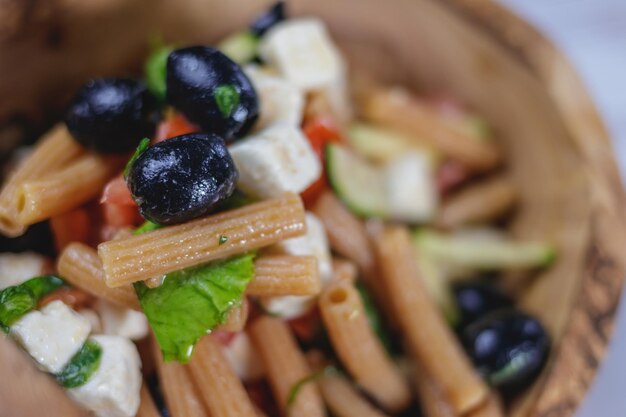 Eine rustikale Holzschüssel mit einem mediterranen Nudelsalat