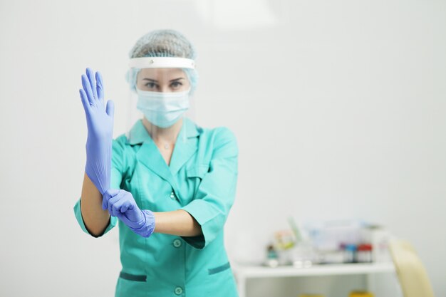 Eine Ärztin in Uniform, medizinischer Maske und Schutzschild zieht Handschuhe an