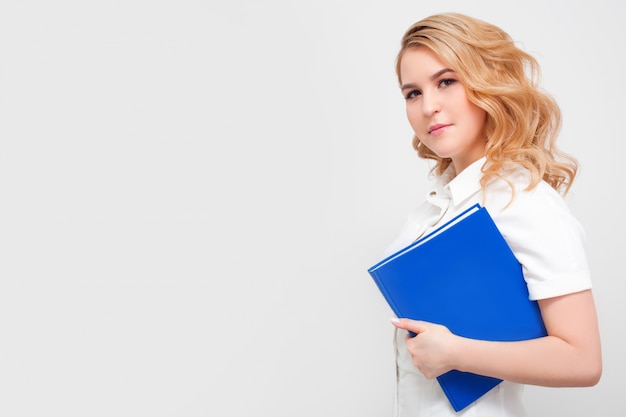 Eine Ärztin mit einem Buch in einer medizinischen Uniform an einer weißen Wand mit Kopierraum. Konzept der medizinischen Ausbildung, Hochschulbildung, Lesen von Büchern und Arztberuf.