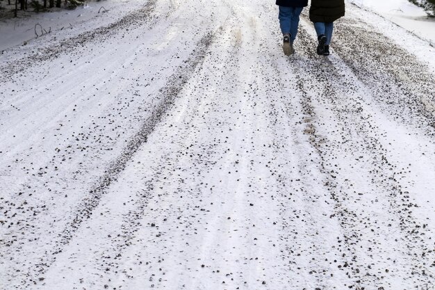 Eine sandige Schotterstraße mit weißem Schnee und Menschenbeinen