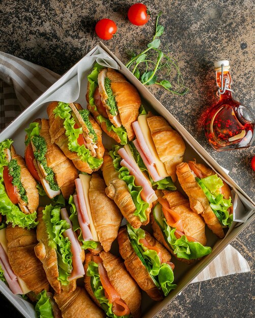 Eine Schachtel voller frisch zubereiteten Croissant-Sandwiches mit Schinken, Käse, Salat und Tomaten